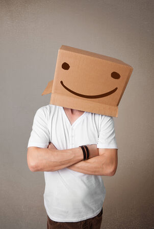 Young man standing and gesturing with a cardboard box on his head with smiley faceの写真素材