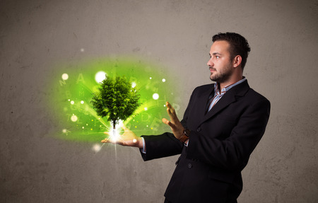 Young businessman holding a glowing tree in his handの写真素材