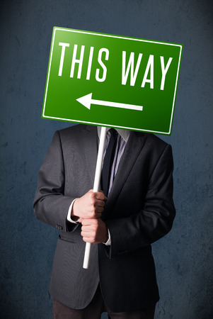 Businessman standing and holding a green direction sign in front of his headの写真素材