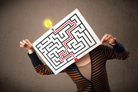 Young woman holding a paper with a labyrinth on it in front of her headの写真素材