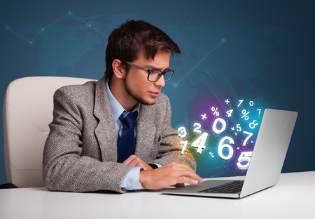 Handsome young man sitting at desk and typing on laptop with 3d numbers comming out