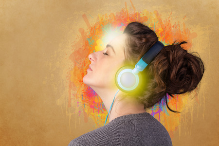Pretty young woman with headphones listening to music in front of a painted wallの写真素材