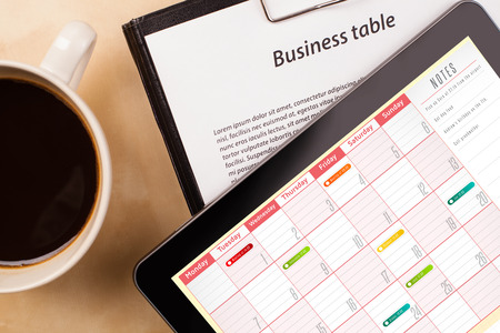Workplace with tablet pc showing calendar and a cup of coffee on a wooden work table close-upの写真素材