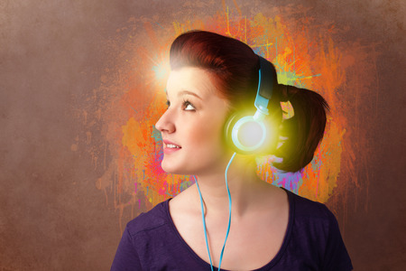 Pretty young woman with headphones listening to music in front of a painted wallの写真素材