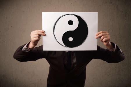 Businessman holding a paper with a yin-yang symbol on it in front of his headの写真素材