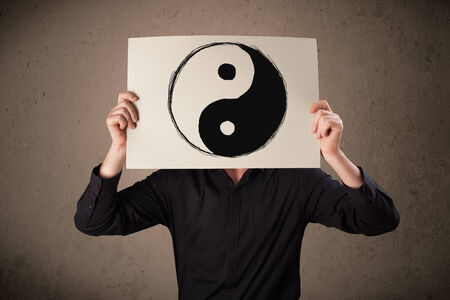 Businessman holding a paper with a yin-yang symbol on it in front of his headの写真素材