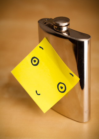 Drawn smiley face on a post-it note sticked on a hip flaskの写真素材