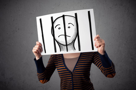 Woman holding a paper with a prisoner in jail behind the bars on it in front of her headの写真素材