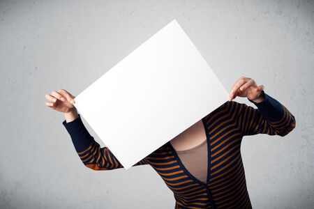 Woman standing and holding in front of her head a white paper with copy spaceの写真素材