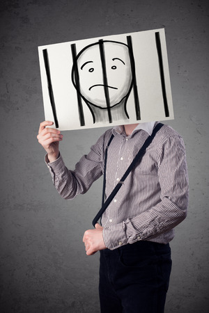 Businessman holding a paper with a prisoner in jail behind the bars on it in front of his headの写真素材