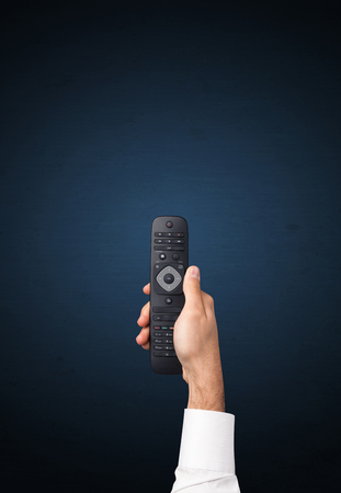 Hand holding a remote control on blue backgroundの写真素材