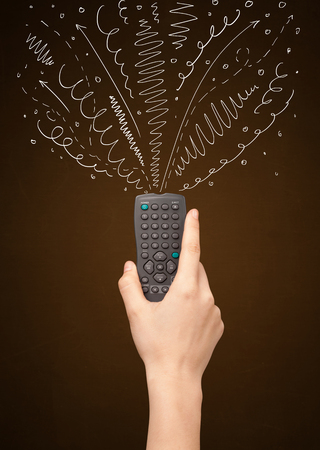 Hand holding a remote control, curly lines and arrows coming out of itの写真素材