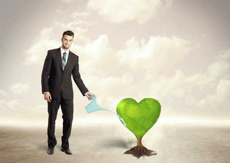 Business man watering heart shaped green tree concept on backgroundの写真素材