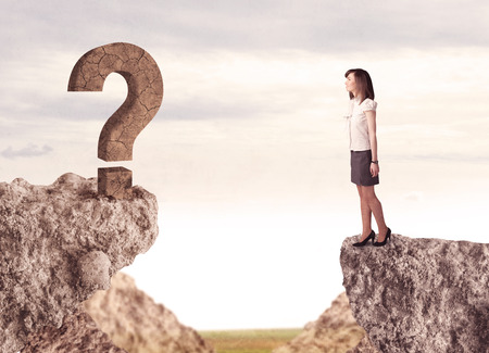 Businesswoman standing on the edge of mountain with a rock question mark on the other sideの写真素材