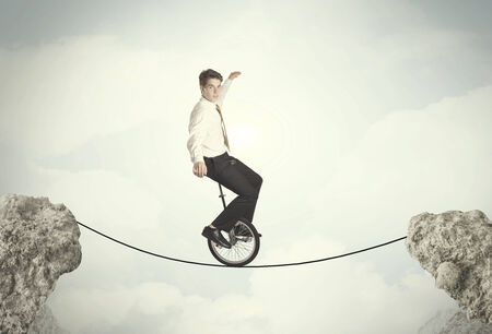 Brave business man riding an mono cycle between cliffs conceptの写真素材
