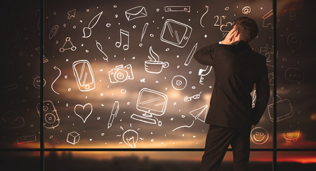 Businessman drawing media icons on glass window, bokeh cityscape backgroundの写真素材