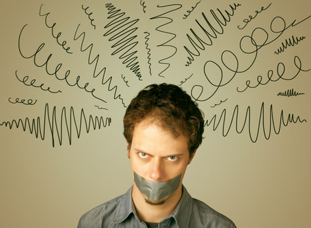 Young man with taped mouth and curly lines around his headの写真素材
