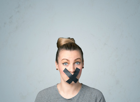 Young woman with taped mouth. Isolated on gray backgroundの写真素材