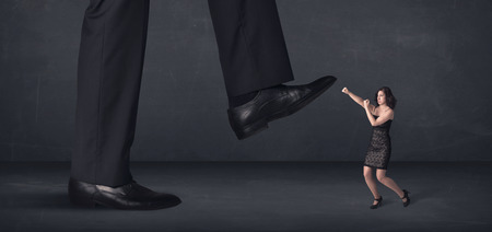 Giant person stepping on a little businesswoman concept on backgroundの写真素材