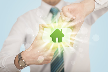 Hands creating a form with shining green house in the center