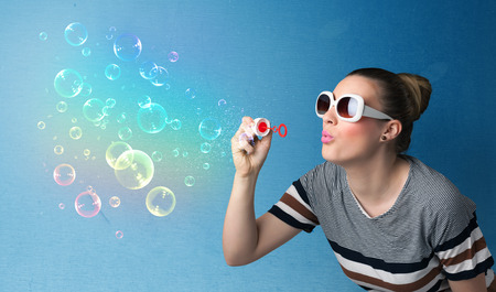 Pretty lady blowing big colorful bubbles on blue background