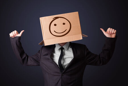 Businessman standing and gesturing with a cardboard box on his head with smiley faceの写真素材
