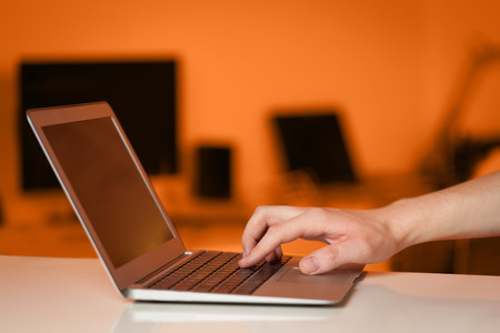 Businessman pressing modern laptop computer on colorful office backgroundの写真素材