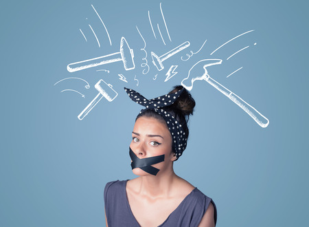 Young woman with taped mouth and white drawn beating hammer marks around her headの写真素材