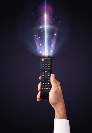 Hand holding a remote control, shining numbers and letters coming out of itの写真素材