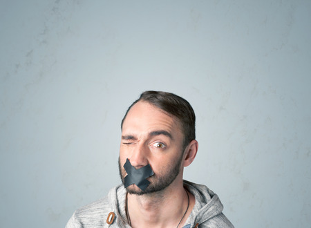 Young man with taped mouth. Isolated on gray background