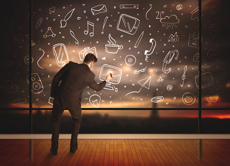 Businessman drawing media icons on glass window, bokeh cityscape backgroundの写真素材