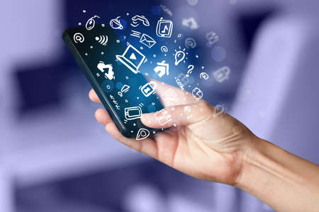Hand holding smartphone with media icons and symbol collection