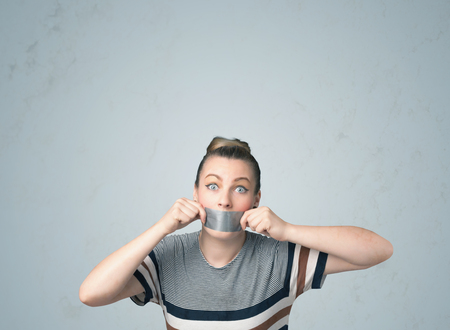 Young woman with taped mouth. Isolated on gray backgroundの写真素材