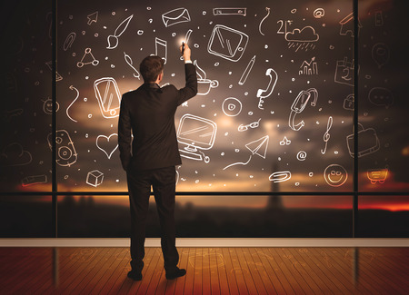 Businessman drawing media icons on glass window, bokeh cityscape backgroundの写真素材