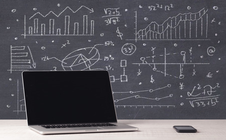 An elegant office desktop with portable laptop and drawn pie charts, graphs, numbers in the background conceptの写真素材