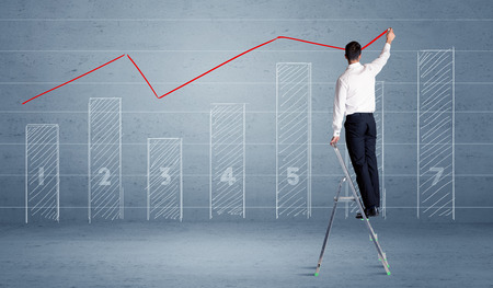 A man in elegant suit standing on a small ladder and drawing a chart on blue wall background with numbers, lines, blocks,の写真素材