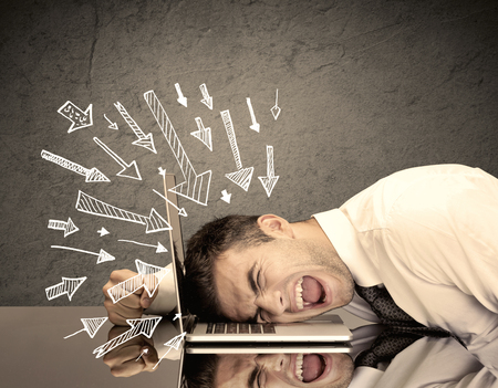 An exhausted business person resting his head on keyboard with pressure illustrated by arrows pointing at him conceptの写真素材