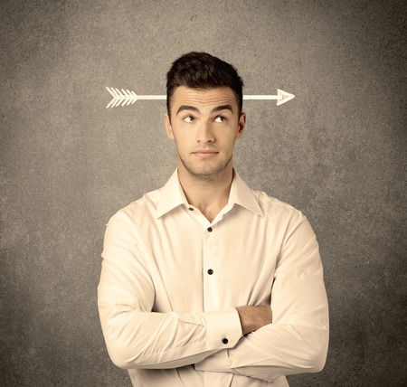 A confused young business guy giving thumbs up with a drawn arrow going through his head conceptの写真素材