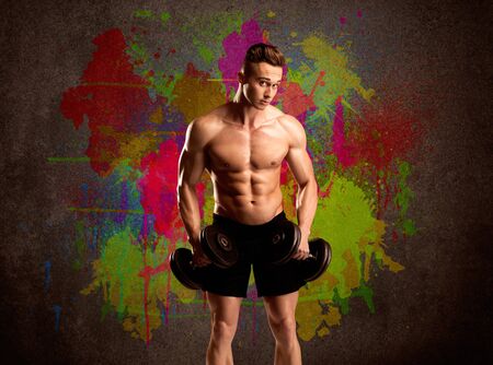 A muscular young bodybuilder lifting weight and showing his hot body with muscles in front of an urban painted wall conceptの写真素材