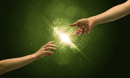 Two naked male hands about to touch, lighting the spark with modest explosion in front of green background conceptの写真素材