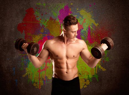A muscular young bodybuilder lifting weight and showing his hot body with muscles in front of an urban painted wall conceptの写真素材