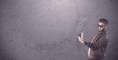 A stylish funny hipster person holding a vintage camera and taking photographs in front of a...