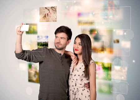 Collecting memories concept with photos in backbround and a happy young couple in love taking selfie with a mobile phoneの写真素材