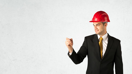A young architect in red safety helmet planning and drawing with a pen in his hand in empty space in front of a white background.の写真素材