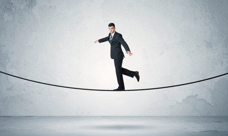 A confident businessman with briefcase walking ahead on a tightrope in empty grey urban space conceptの写真素材