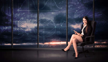 Businesswoman holding tablet in office room with graph charts on window conceptの写真素材