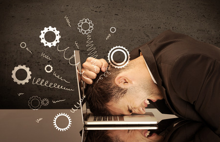 Falling apart illustration concept with cranks, cog wheels springing from a fed up and tired businessman's head resting on laptop keyboardの写真素材