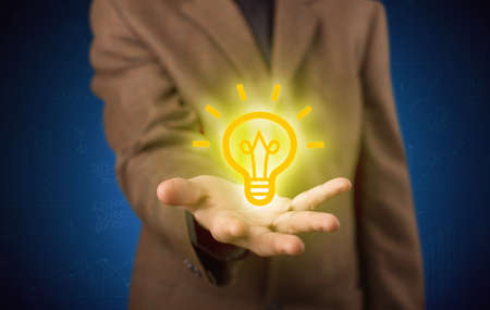 A creative businessman has a great bright idea illustrated by holding a drawn light bulb in the hand conceptの写真素材