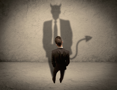 An experienced tricky businessman in suit looking at his devil desguise shadow reflected on the wall conceptの写真素材