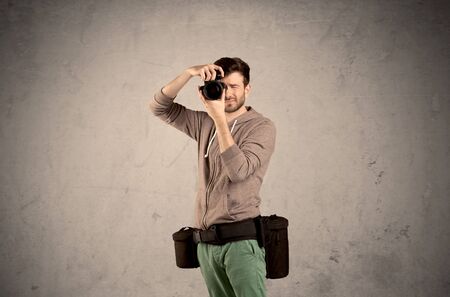 A professional male photographer with belt holding a camera and taking photos in front of clear grey...